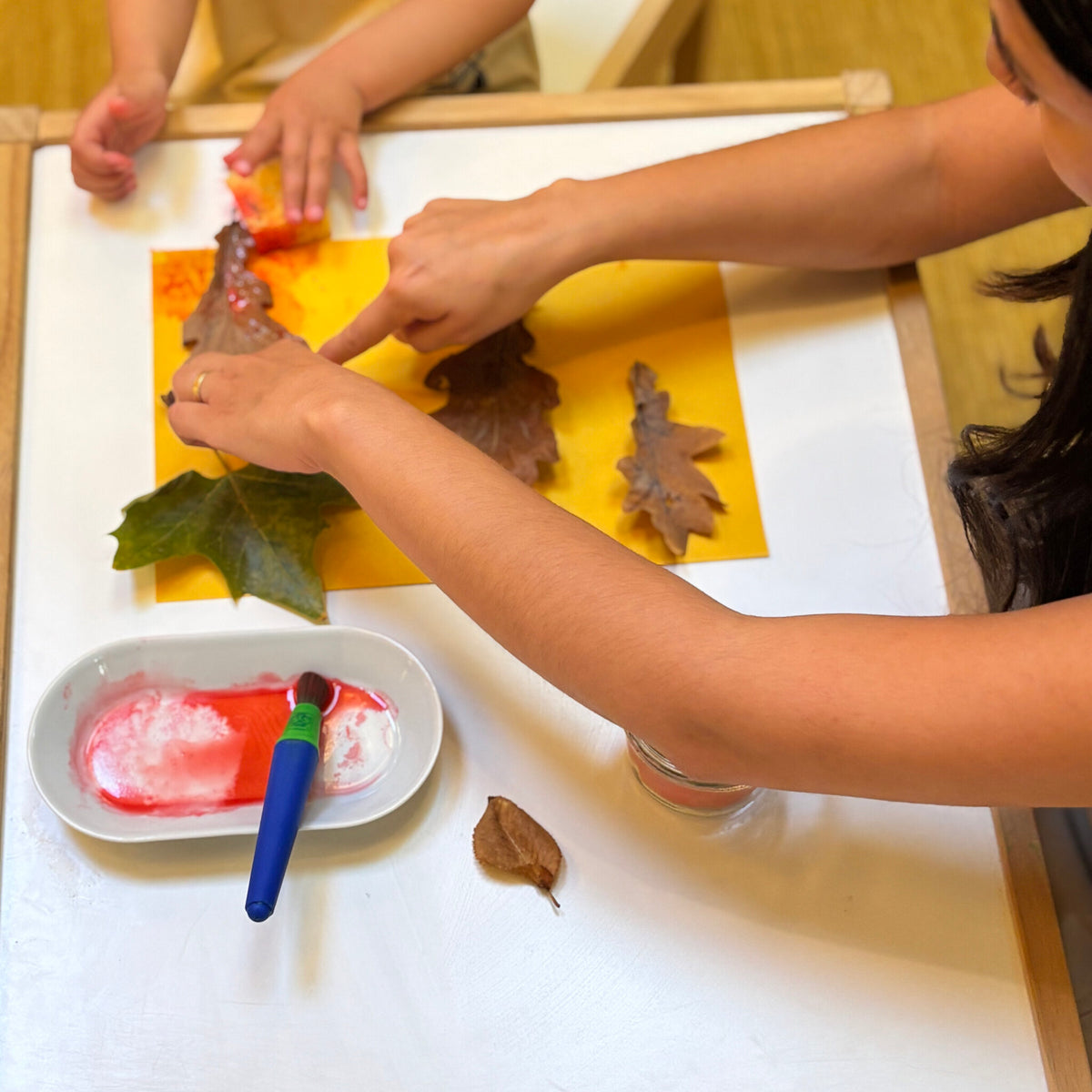 Petites mains pressant des feuilles d’automne peintes sur du papier jaune